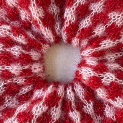 A close-up of a red and white patterned knit fabric with a circular opening in the center, showing a fuzzy, textured yarn.